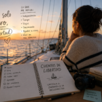 Mujer mirando el horizonte desde un velero al atardecer, con un cuaderno que dice "Cuentos de Libertad - Capítulo 1: Zarpando a lo desconocido", libros de desarrollo personal y notas con motivaciones personales